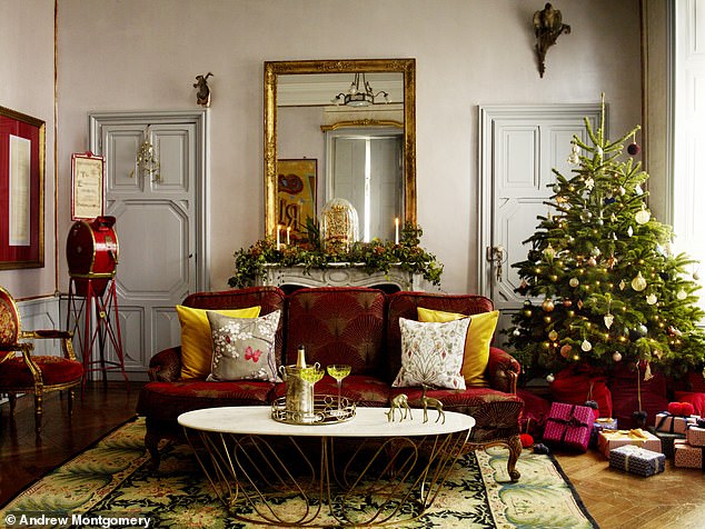 Elegant living room with a festive Christmas tree, red chenille upholstered sofa, gold accents, and a decorative mirror above a mantelpiece.