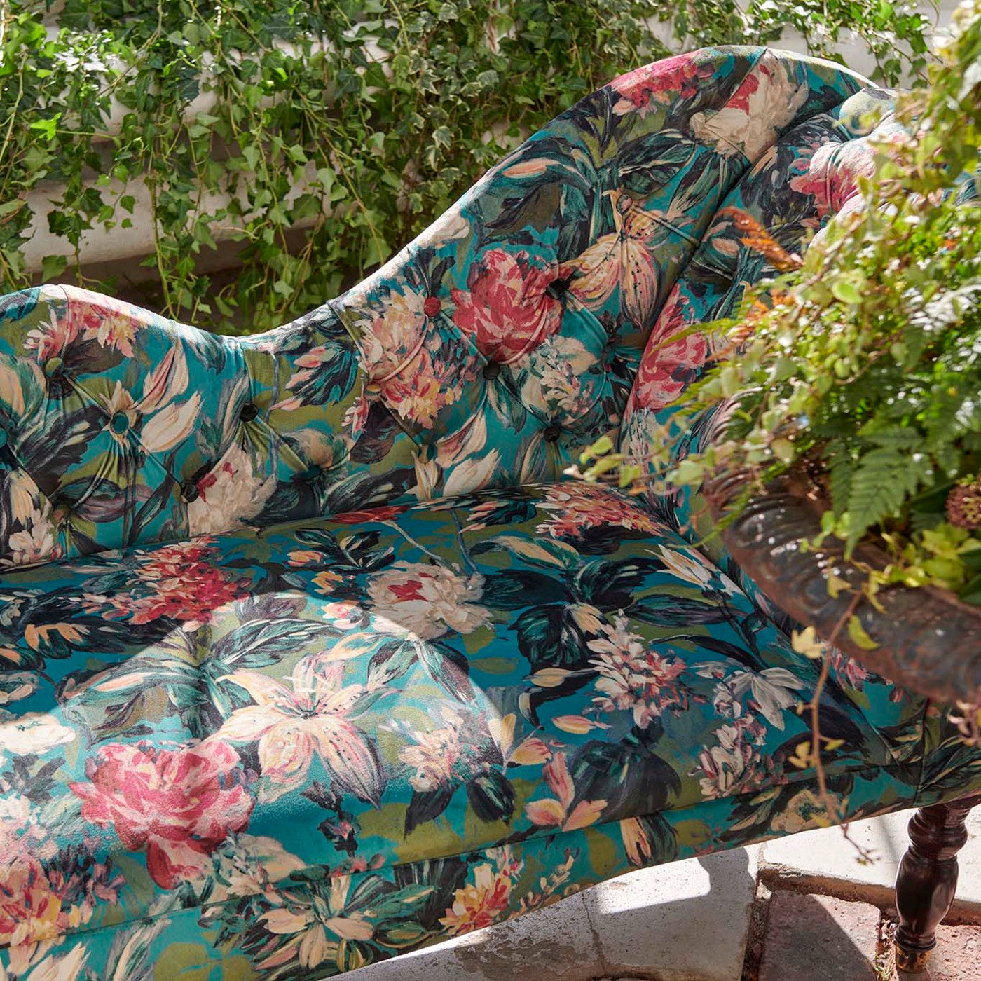 Upholstered chaise lounge with Botanical Blooms Velvet Peacock fabric showcasing bold floral designs in a lush garden setting.