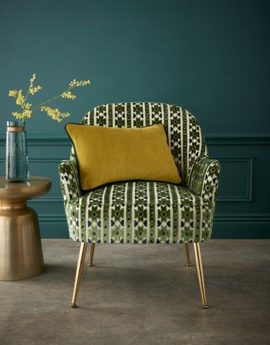 Elegant armchair with African-inspired green patterned fabric, paired with a mustard cushion, set against a deep green wall and gold side table.