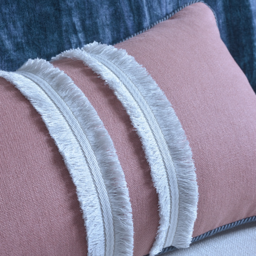 Close-up of a pink pillow with white fringe trim on a blue textured background