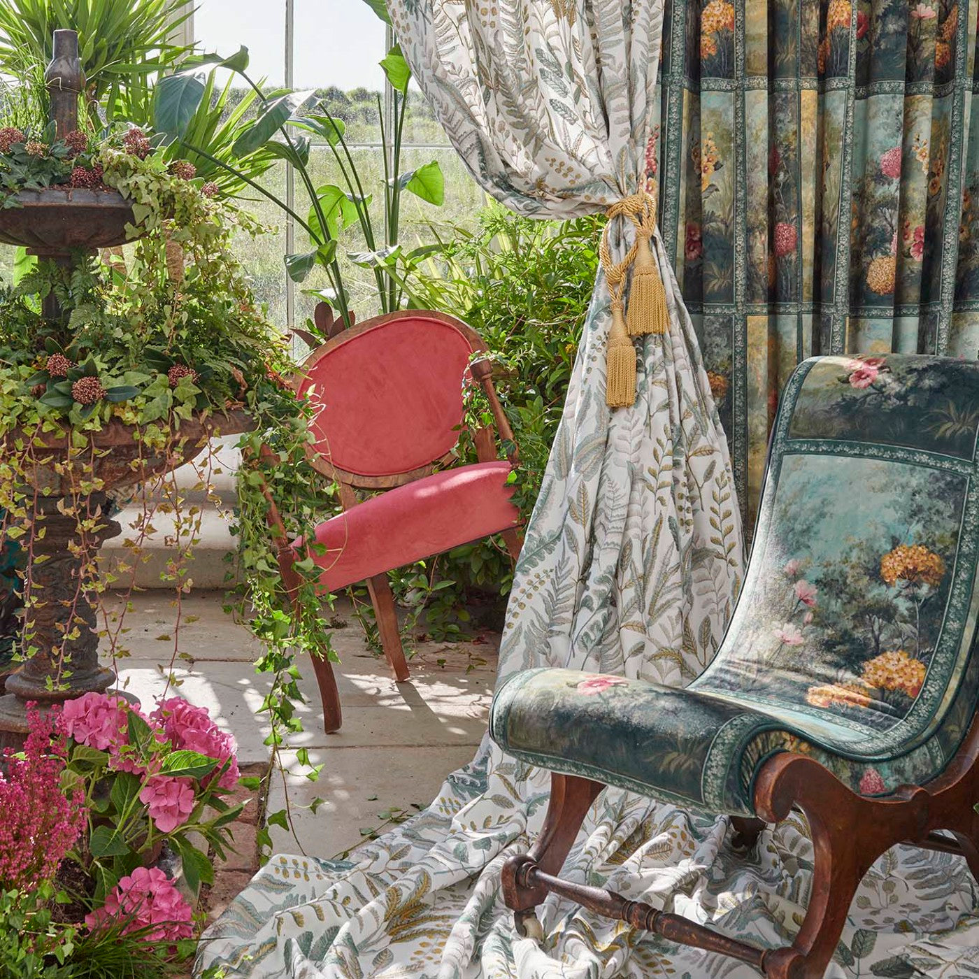 Kew Velvet Forest fabric used in home décor, with curtains and upholstery showcasing floral patterns amidst a garden setting with vibrant plants.