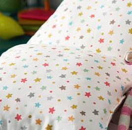 Starburst Multi kids fabric used on bedding, showcasing vibrant multicolour stars on soft white cotton, perfect for playful bedroom décor.