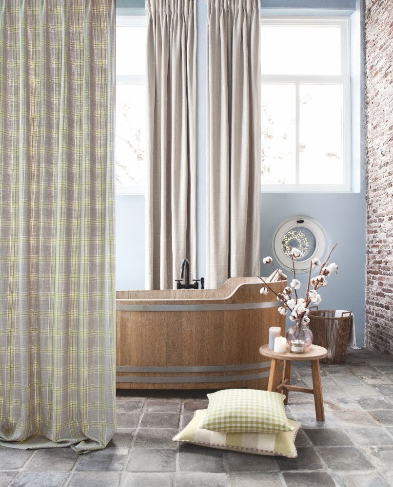 Bathroom décor with Beechwood Moss gingham fabric pillows, neutral linen curtains, and a wooden bathtub in a rustic setting.