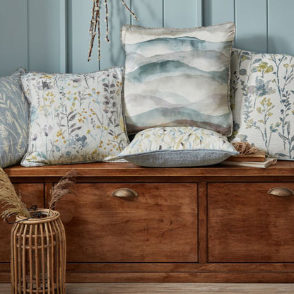 Home décor setup with cushions made from Floral Croft Cornflower fabric, showcasing its blue and pastel floral design in a cosy wooden bench setting.